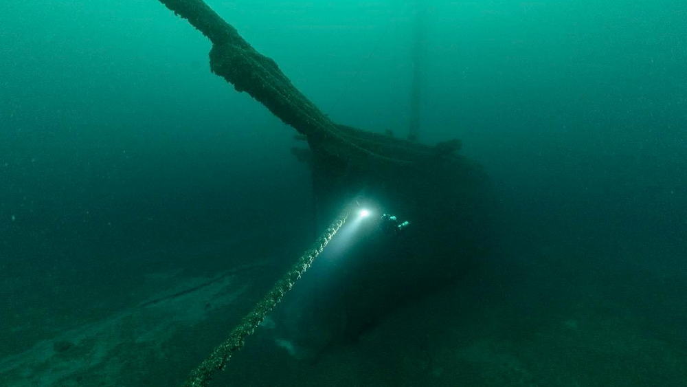 A small diver with light in front of the massive bow of schooner in Lake Michigan